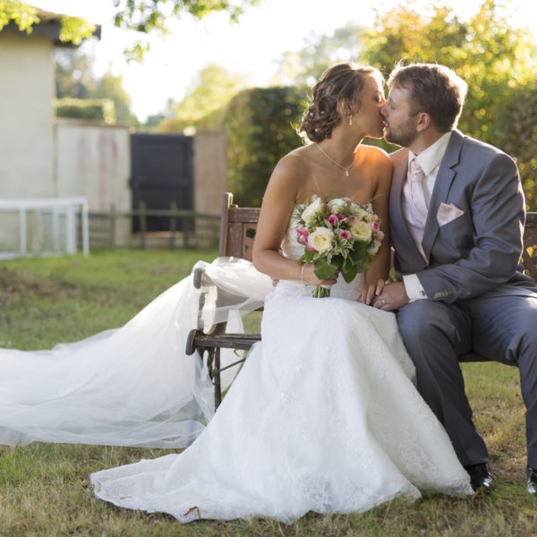 superpe-photo-de-couple-de-jeunes-maries-sur-un-banc-chateau-bordelais-embrassent-bouquet-de-fleurs-robe-a-traine-lumiere-canon-eos-5d-mark-iii-sebastien-huruguen-photographe-mariage-bordeaux