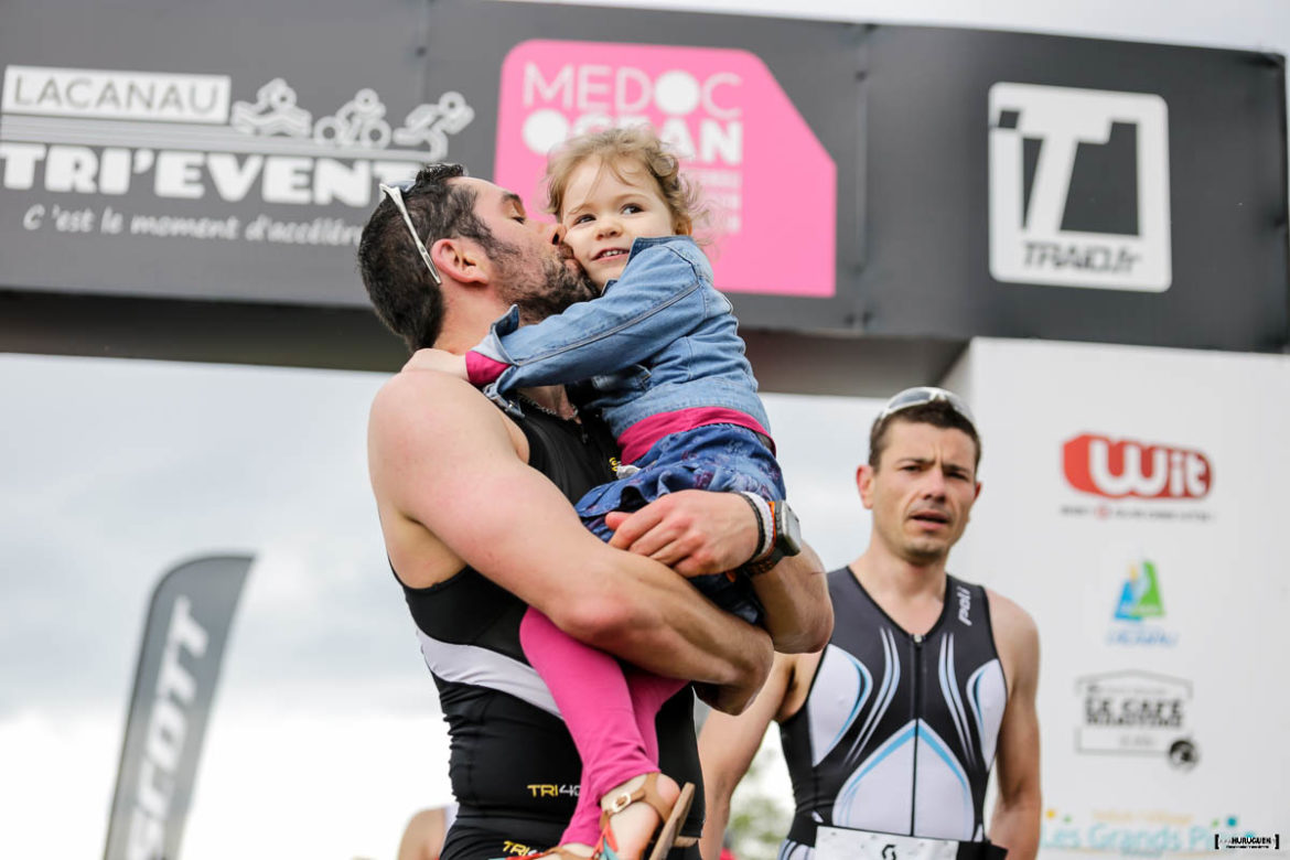 Papa qui termine sa course avec sa fille dans les bras sur la ligne d'arrivée du Scott Half Triathlon - Lacanau Tri Events 2016 | Sébastien Huruguen www.huruguen.fr