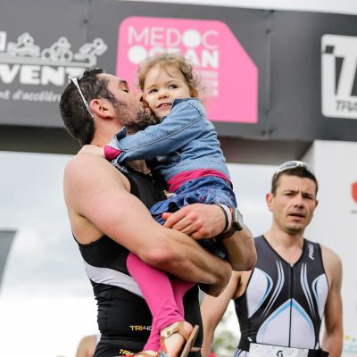 Papa qui termine sa course avec sa fille dans les bras sur la ligne d'arrivée du Scott Half Triathlon - Lacanau Tri Events 2016 | Sébastien Huruguen www.huruguen.fr