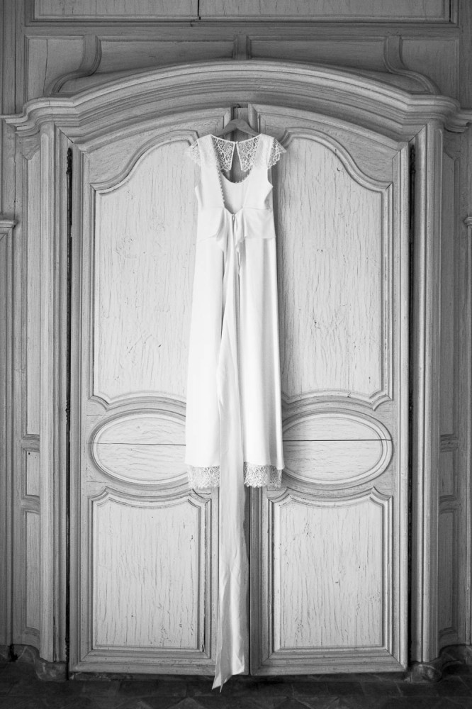 mariage, bordeaux, aquitaine, gironde, sebastien huruguen, photographe mariage, photographe mariage bordeaux, robe de mariage, robe de mariée, robe blanche, porte en bois, vieille porte, belle photo de robe de mariée en noir et blanc suspendue sur un cintre accroché en haut de la porte d'un beau chateau